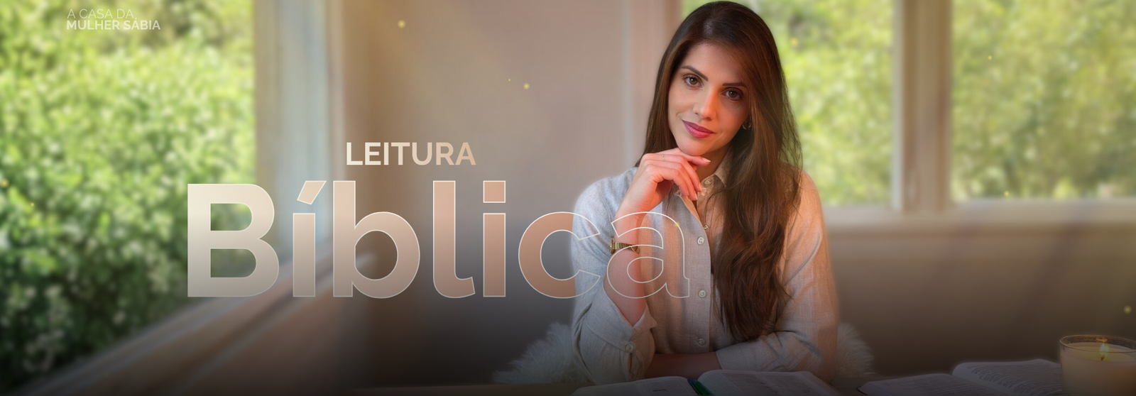 Banner horizontal em tons suaves e naturais. No canto superior esquerdo, em letras pequenas e brancas, aparece o texto “A CASA DA MULHER SÁBIA”. À esquerda da imagem, em destaque, está o texto “LEITURA” em letras menores e claras. Logo abaixo, ocupando grande parte da largura, a palavra “Bíblica” aparece em letras grandes, claras e semitransparentes, sobrepostas ao fundo. À direita, uma mulher adulta está sentada próxima a uma janela, olhando diretamente para quem observa, com expressão calma e acolhedora. Ela tem pele clara, cabelos longos e lisos em tom castanho, repartidos de lado e caindo sobre o ombro direito. Veste uma camisa clara de mangas longas, com botões, e usa um relógio no pulso esquerdo. Sua mão direita apoia levemente o queixo, em gesto de reflexão. À frente dela, na parte inferior da imagem, há um livro aberto sobre a mesa, com páginas visíveis, sugerindo leitura. Ao lado do livro, à direita, aparece uma vela acesa em um recipiente de vidro, emitindo luz suave. O fundo mostra grandes janelas com vista para uma área externa verde, com árvores desfocadas e iluminação natural abundante. Pequenos pontos de luz dourados aparecem espalhados pela imagem, reforçando um clima de serenidade, contemplação e espiritualidade.